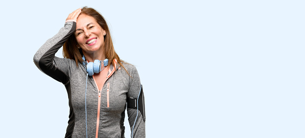 Middle age gym fit woman with workout headphones terrified and nervous expressing anxiety and panic gesture, overwhelmed isolated blue background