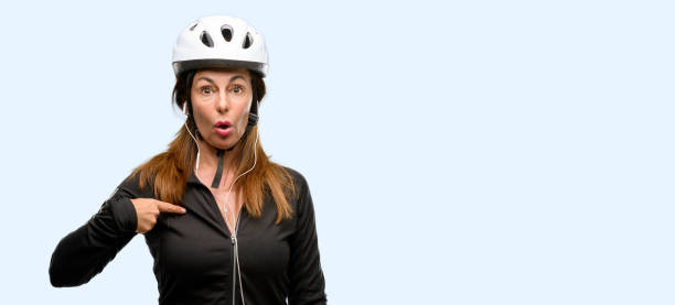 istock Middle age cyclist woman using earphones happy and surprised cheering expressing wow gesture, pointing with finger 1042020604