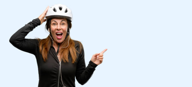 istock Middle age cyclist woman using earphones pointing away side with finger 1042020668