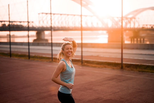 Smiling young fit girl on early morning jogging waving at her friend.