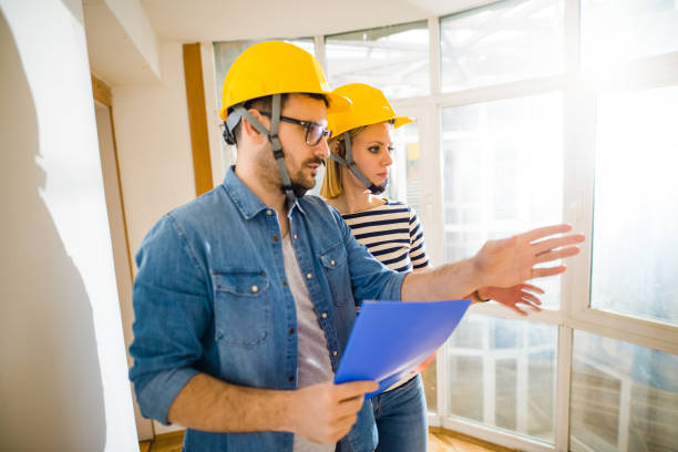 istock Two focused young architects with helmets on their heads looking at projects and shoving on wall. 1042053842
