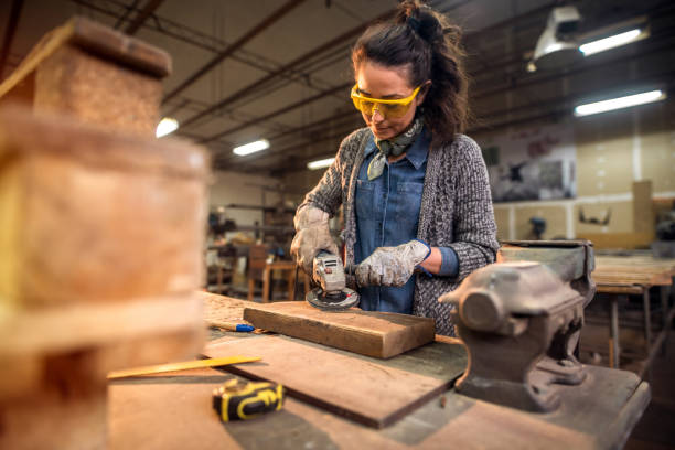 Middle aged professional female carpenter working with sandpaper in her workshop.