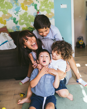 Mother having fun with her three little boys on the floor at home