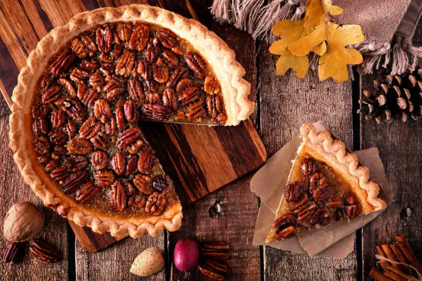 Autumn pecan pie, overhead table scene with cut slice on a rustic wood background