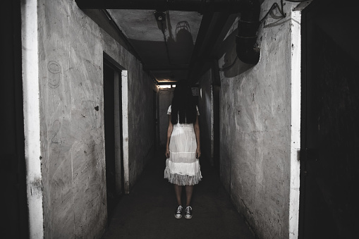 Scary girl in night gown in a dark basement hallway