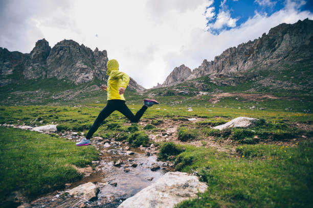 istock Woman trail runner jumping over samll river on beautiful mountains 1042103376