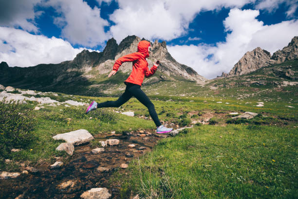 istock Woman trail runner jumping over samll river on beautiful mountains 1042103726