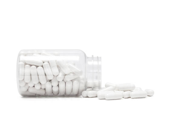 白い薬のカプセルは透明ボトルからこぼれる - capsule pill white nutritional supplement ストックフォトと画像