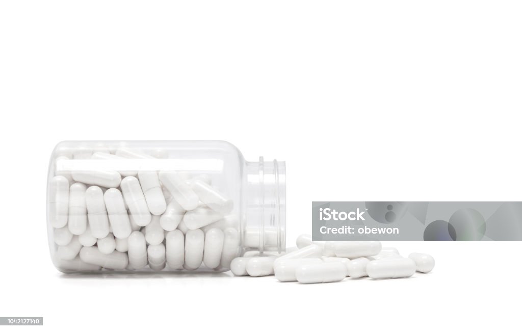 white medicine capsules spill out from transparent bottle white medicine capsules spill out from transparent bottle and isolated on white background Capsule - Medicine Stock Photo