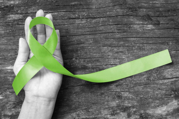 лимфома рака осведомленность лайм зеленая цветная лента на руку на старом возрасте деревянный фон: сатин ткани символический логотип повы� - lyme disease стоковые фото и изображения