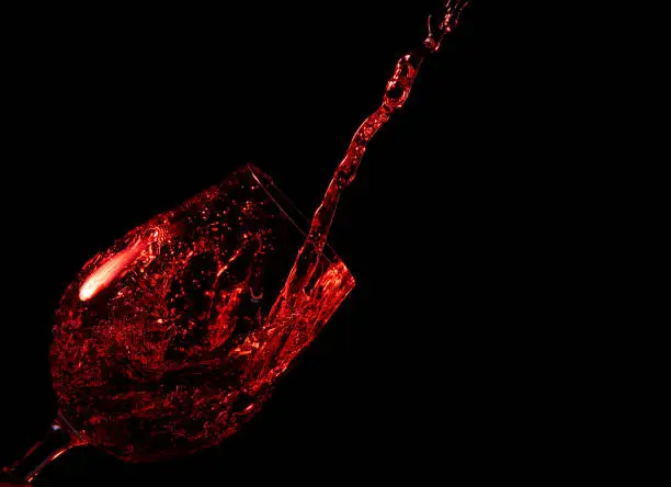 Pouring red wine into a glass on a black background