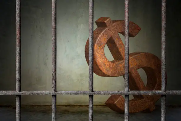Photo of Large rusty dollar sign is imprisoned in old prison rusted metal bars