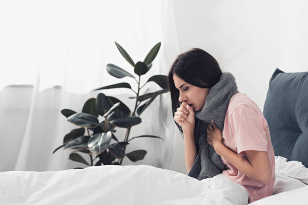 istock sick young woman sitting in bed and having cough while suffering from sore throat 1042298228