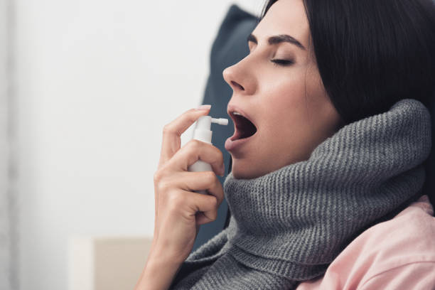 istock sick young woman in scarf using cough spray 1042300916