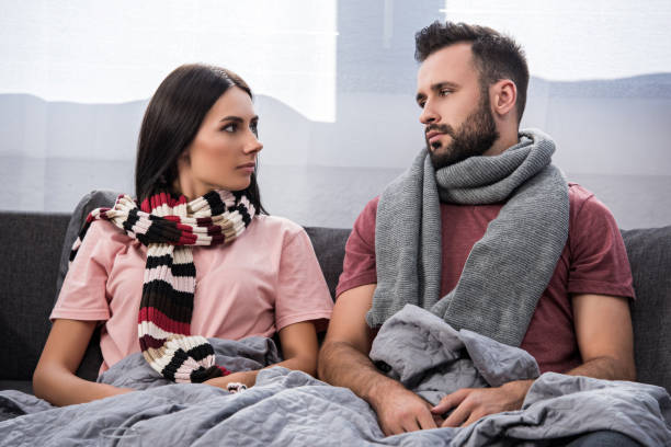 istock sick young couple sitting on couch and looking at each other 1042305402