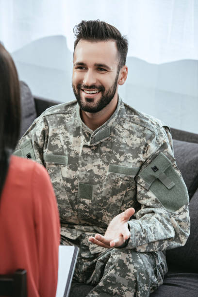 istock smiling soldier talking at psychiatrist and gesturing while sitting on couch during therapy session 1042305464