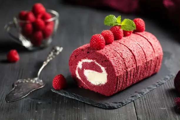 Red velvet Sponge Swiss roll with fresh raspberry on dark background
