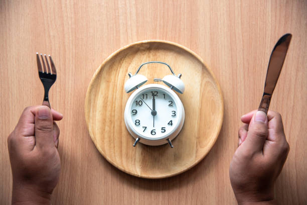 l'orologio è alle 12:00 per pranzo in un piatto di legno. - ore 12:00 foto e immagini stock