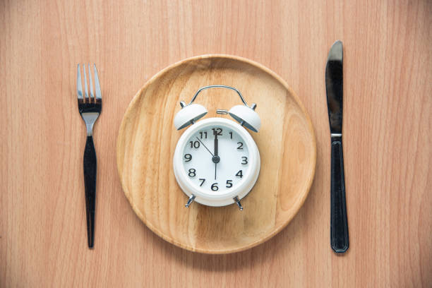 l'orologio è alle 12:00 per pranzo in un piatto di legno. - ore 12:00 foto e immagini stock