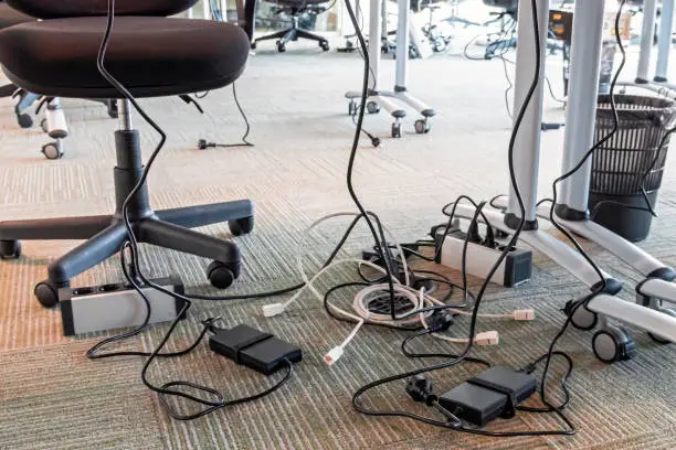 Photo of Concept of clutter in office. Unwound and tangled electrical wires under the table. 5S system of lean manufacturing.