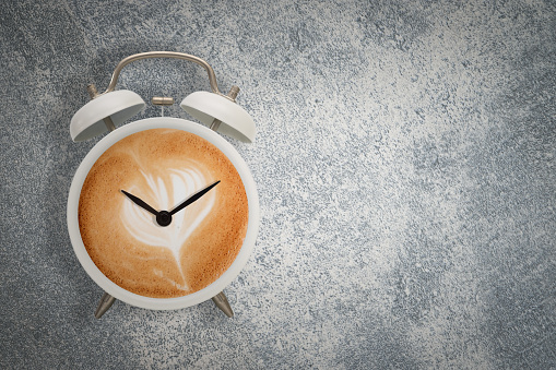 Hot coffee with frothy foam in white alarmclock design is Coffee Time Concept.