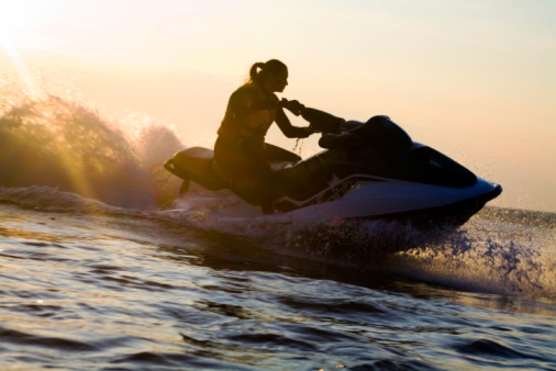 beautiful girl riding her jet skis in the sea at sunset. silluet. spray