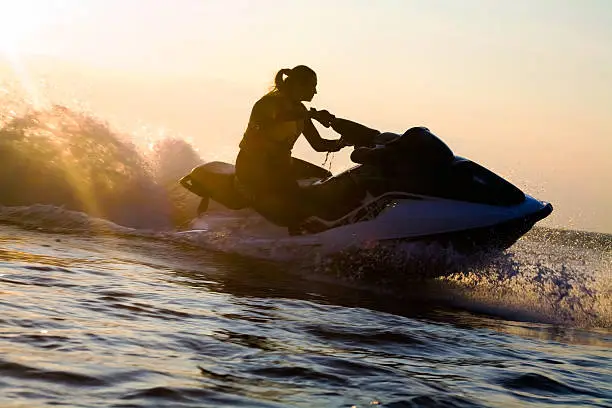 beautiful girl riding her jet skis in the sea at sunset. silluet. spray