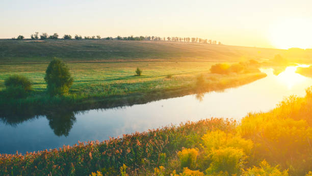 istock Sunny summer landscape with river flowing between green hills,fields and meadows.Sunrise.Quiet morning.Calm.Warm sunlight.Cloudless clear blue sky. 1042379400