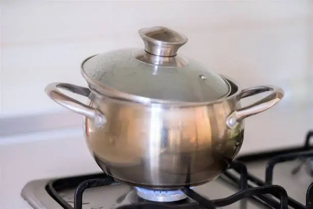 A stainless steel pan with a slightly opened lid during cooking on a gas stove