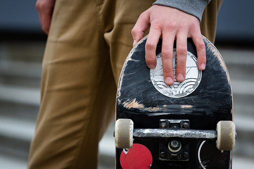 Skater hand holding skateboard deck in an urban surroundings outdoors