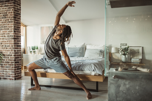 Young men practicing yoga at home. He is in bedroom and doing yoga, first thing in the morning.