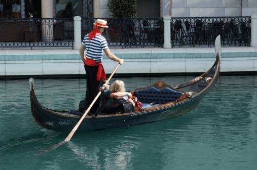 Venice, Italy - February 20, 2022: A Venetian gondolier expertly navigates his gondola and passengers through the narrow canals of Venice, Italy.