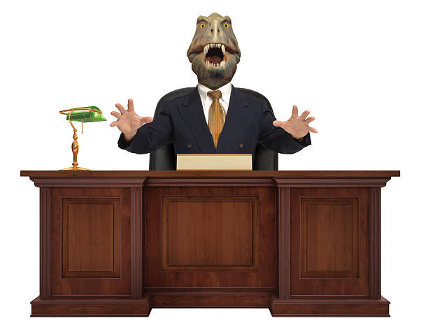 T-Rex head on a businessman's body sitting behind a desk stock photo