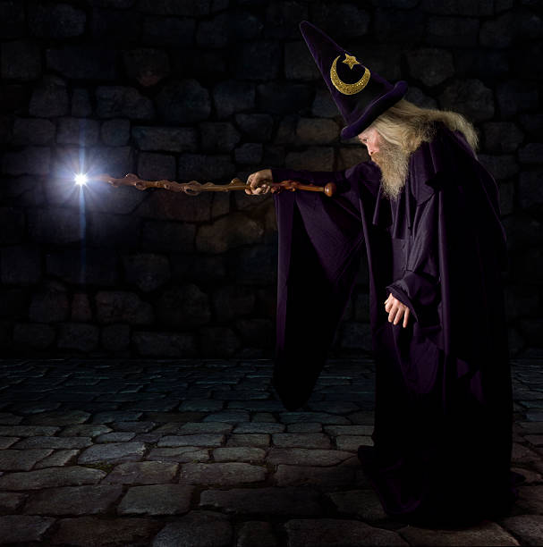 A wizard pointing his glowing wand Wizard in a purple robe and wizard hat casting a spell with his wand merlin the wizard stock pictures, royalty-free photos & images