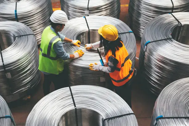 Aerial view of young engineer man and industrial worker woman checking production line and testing quality of steel pipe coils at warehouse section in cable factory. XXXL