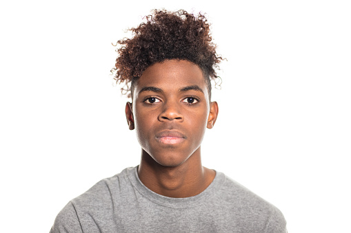 Close-up portrait of serious looking teenager. African teenage boy looking at camera against white background.