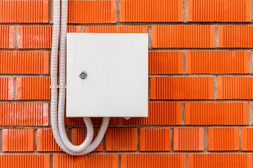 A white box with an electric high-voltage cable on a red brick wall with copy space.