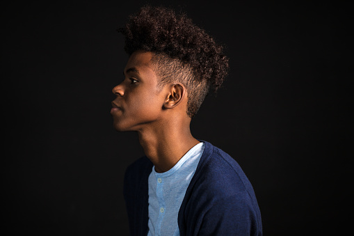 Side portrait of young boy with afro hair style on black background. African boy in casuals in studio.