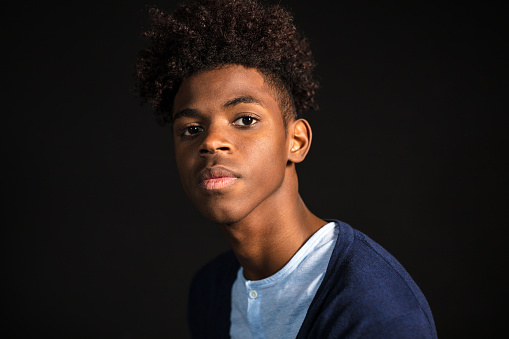 Close-up portrait of confident young man in casuals looking at camera. Teenager with afro hair on black background.