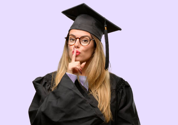 istock Young woman university graduate student with index finger on lips, ask to be quiet. Silence and secret concept 1042425274