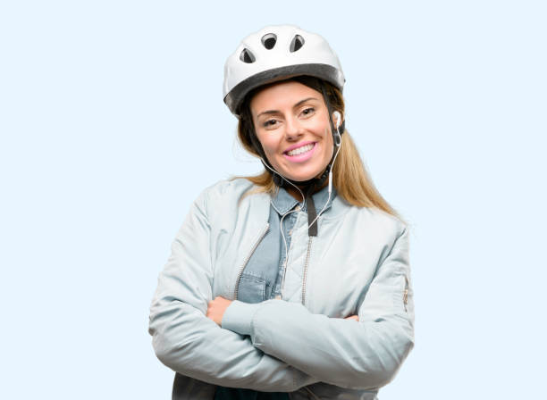 молодая женщина с велосипедным шлемом и наушниками со скрещенными руками уверенно и счастлива с большой естественной улыбкой смеха - arms crossed audio стоковые фото и изображения
