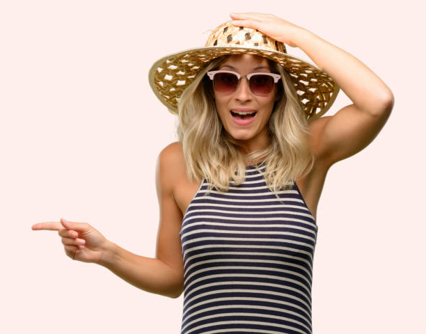 istock Young woman using sunglasses wearing summer hat pointing away side with finger 1042437128