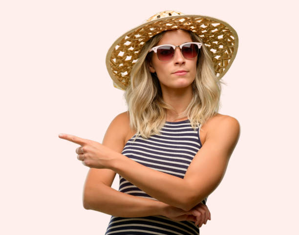 istock Young woman using sunglasses wearing summer hat pointing away side with finger 1042437172