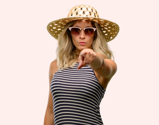 istock Young woman using sunglasses wearing summer hat pointing to the front with finger 1042437190