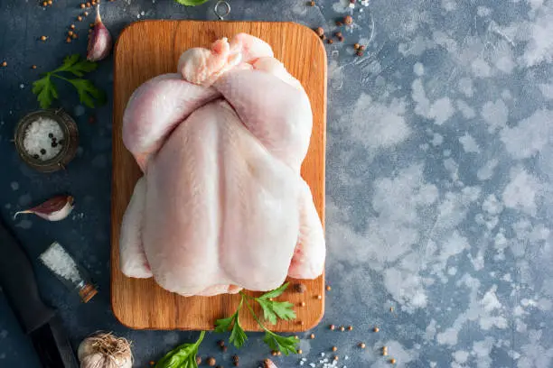 Photo of Whole raw chicken on a wooden board with spices for cooking, top view, horizontal, copy space