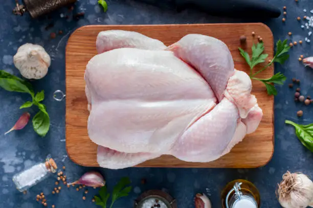 Photo of Prepared fresh raw chicken for cooking on a cutting wooden board, top view, selective focus