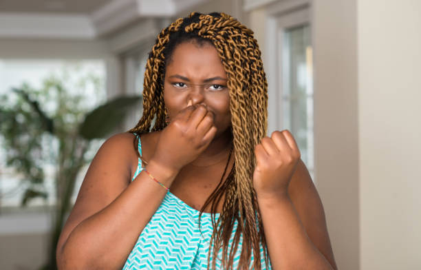 une femme afro-américaine à domicile sentant quelque chose de puante et dégoûtante, odeur intolérable, retenant le souffle avec les doigts sur le nez. concept de mauvaises odeurs. - disgust women african ethnicity human face photos et images de collection