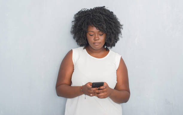 istock Young african american woman over grey grunge wall texting a message using smartphone with a confident expression on smart face thinking serious 1042447512