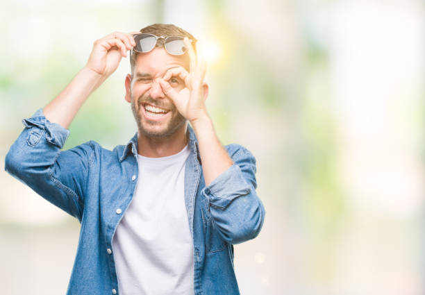 istock Young handsome man wearing sunglasses over isolated background doing ok gesture with hand smiling, eye looking through fingers with happy face. 1042450914