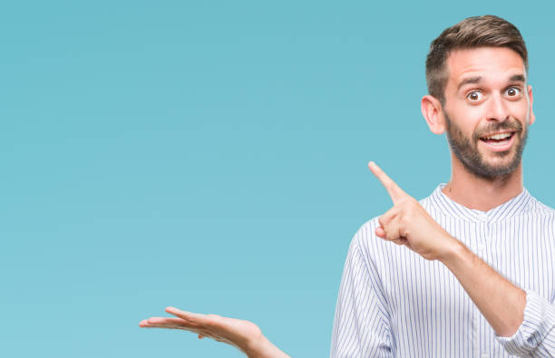 istock Young handsome man over isolated background amazed and smiling to the camera while presenting with hand and pointing with finger. 1042451142